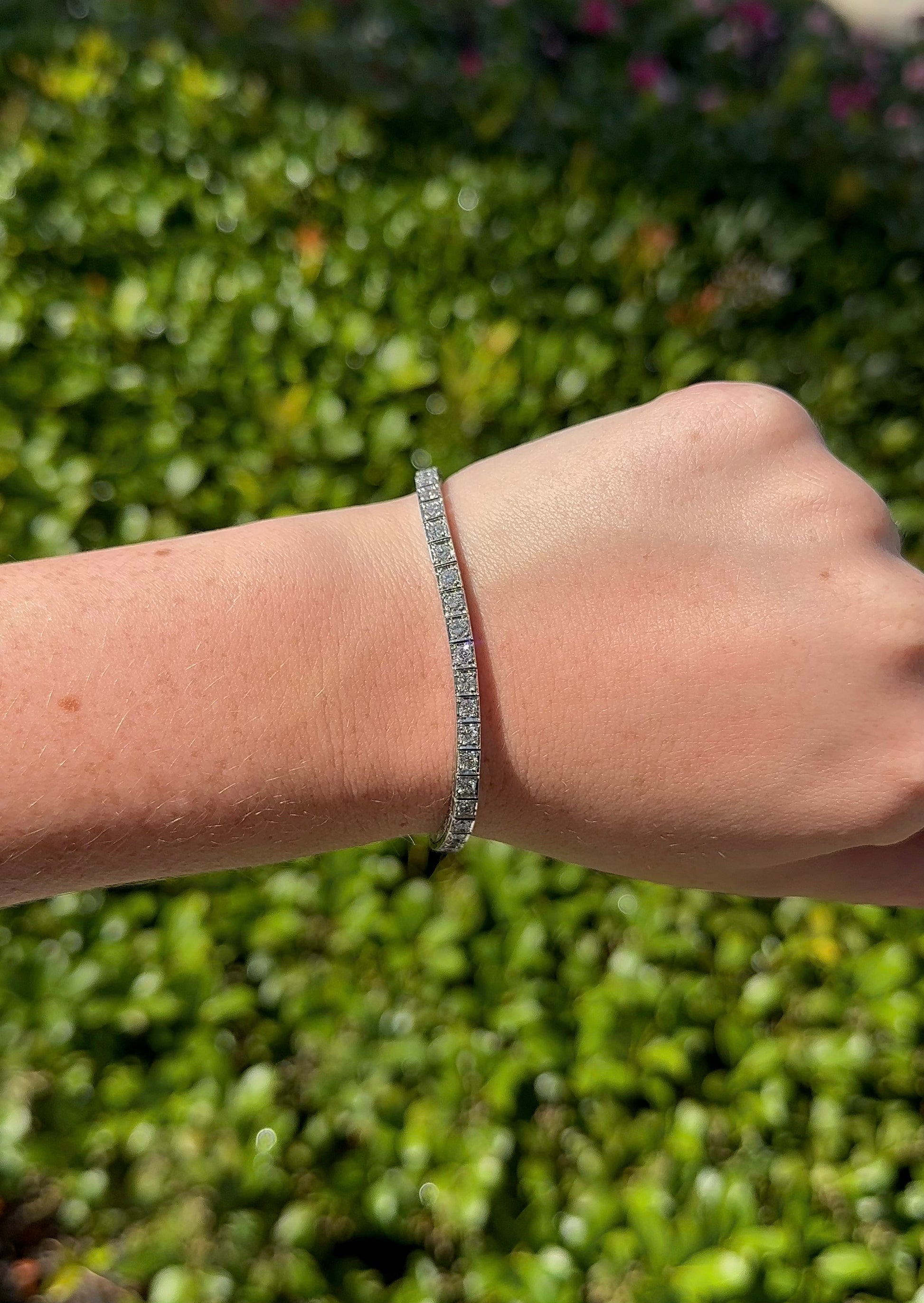 Hand wearing a bracelet with a green leafy background