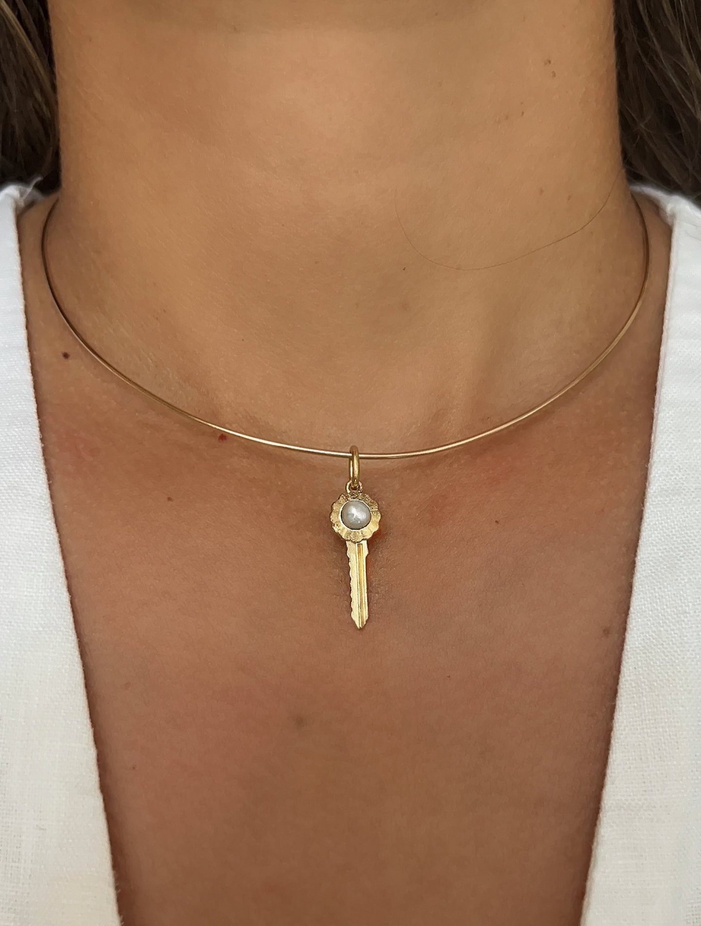 Gold wire necklace with a pearl key pendant on a person wearing a white top.
