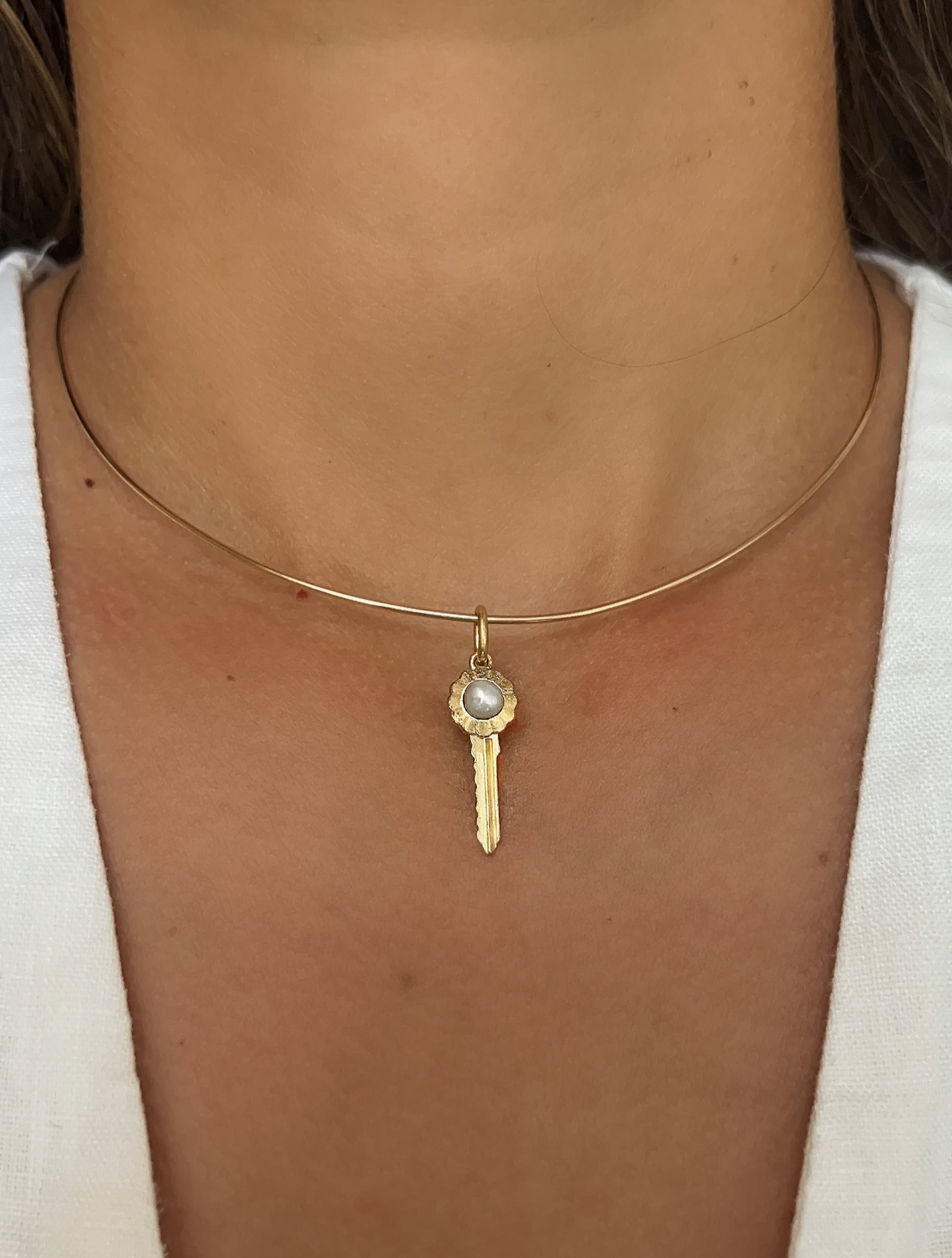 Gold wire necklace with a pearl key pendant on a person wearing a white top.